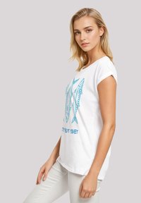 White cotton t-shirt with blue fish graphic and text "Sassy but Sweet," short sleeves, and relaxed fit. Smooth texture, slightly curved hem.