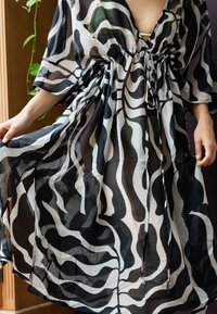 Transparante zwart-witte kaftan met golvende abstracte patronen in groene en donkere tinten, met een gathering in de taille en wijde mouwen.