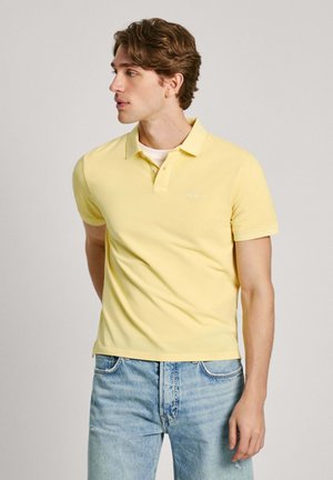 Żółta koszulka polo o slim fit, krótki rękaw i kołnierzyk, w połączeniu z jasnoniebieskimi dżinsami. Zawiera haftowane logo na klatce piersiowej.