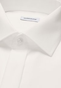 Gros plan sur le col d'une chemise blanche avec un bouton transparent et une étiquette de marque "seidensticker" visible à l'intérieur du col.