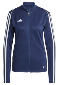Marineblaue Zip-Jacke aus weichem Stoff mit drei weißen vertikalen Streifen an jedem Arm und einem Logo auf der unteren rechten Seite.