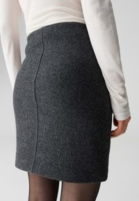 Gonna di lana grigia con design strutturato, orlo leggermente svasato e dettagli di cuciture visibili. Indossata con un top leggero a maniche lunghe e collant.