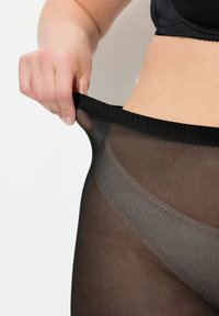 Collant neri con una trama trasparente, tirati da una mano, con un'ampia fascia in vita e una finitura liscia, che si fondono nei toni della pelle.