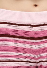 Κλείσιμο εικόνας στην περιοχή της μέσης ενός ατόμου που φορά ριγέ πλεκτό παντελόνι σε ροζ, λευκό και καφέ, με εμφανές τον αφαλό πάνω από τη μέση του παντελονιού.