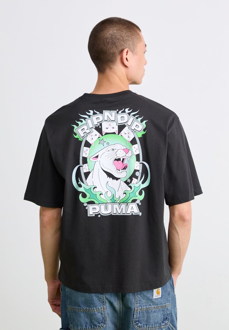 Mand vender væk iført sort skjorte med en brølende hvid pantergrafik omkranset af grønne flammer og teksten "RIPNDIP" og "PUMA".
