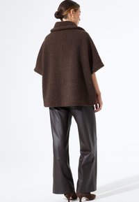 Bruine gewatteerde fleece poncho met een hoge kraag, korte mouwen en een losse pasvorm, gecombineerd met slanke, donkerbruine leren broeken.