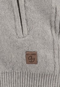 Pullover grigio lavorato a maglia con zip frontale a metà, caratterizzato da una tessitura testurizzata e una patch in pelle marrone con il logo nella parte inferiore sinistra.