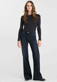 Zwarte langärmige top gecombineerd met donkerblauwe wijde jeans. De jeans hebben een hoge taille en een knoopsluiting. Zachte denim textuur.