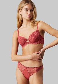 Lace bralette and matching thong in deep rose, featuring scalloped edges, adjustable straps, and a semi-sheer texture with a keyhole design.