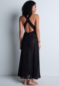 Robe maxi noire et transparente avec un design à dos croisé, dos ouvert et une silhouette fluide. Dotée d'un tissu doux et léger.