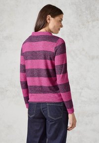 Pull rayé rose et violet foncé avec un col, design ajusté et poignets côtelés, porté avec un jean noir.