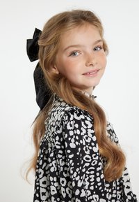 Sort og hvid leopardprint kjole med flæset krave detaljer, præget af langt, bølget hår og en stor sort satin sløjfe som accessorie.