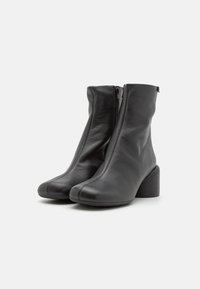 Bottes courtes en cuir noir avec bouts arrondis, fermetures éclair latérales et talons blocs, posées côte à côte sur un fond blanc.