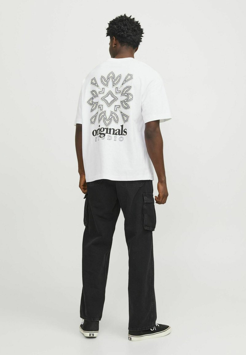 T-shirt bianca in cotone con una grande stampa geometrica nera e il testo "originals STUDIO" sulla parte posteriore, abbinata a pantaloni cargo neri.