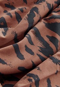 Brun tyg med svart abstrakt leopardmönster, med en mjuk textur och något stretchigt material, vikt för att visa detaljer.