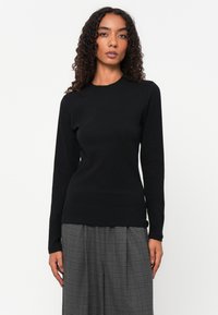 Svart langermet ribbet topp med rund hals, tettsittende form og glatt tekstur, kombinert med rutete vide bukser.