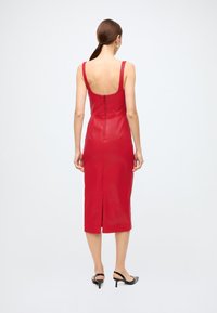 Vestido midi de couro vermelho com costas arredondadas, silhueta justa e fecho de correr nas costas ao centro. Apresenta uma fenda na parte inferior das costas e alças largas nos ombros.