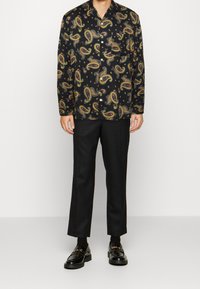 Camisa de botones negra con un colorido patrón de paisley, combinada con pantalones negros de corte recto y mocasines brillantes.