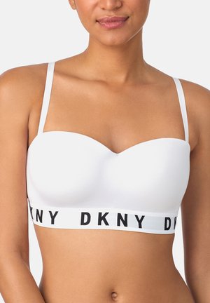 Mujer con un sujetador blanco sin tirantes, con tiras finas y una banda elástica de DKNY con la marca debajo del busto.