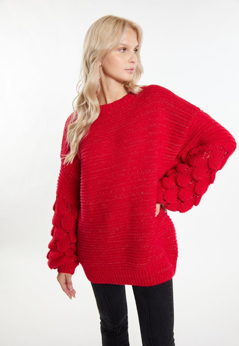 Roter Strickpullover mit übergroßen, strukturierten Ballonärmeln und einem gerippten Saum. Das Material wirkt weich und hat ein voluminöses Design.
