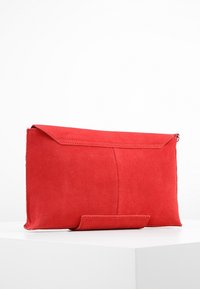 Punot punane suede, millel on lame ristkülikukujuline kuju, silmapaistva siledaga tekstuur, nurga all klapi sulgemine ja nähtavaid metallkomponente pole.