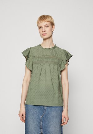 Top court à manches courtes vert avec volants, un col rond et un motif à pois texturé. Présente des détails froncés au niveau de la poitrine et des épaules.
