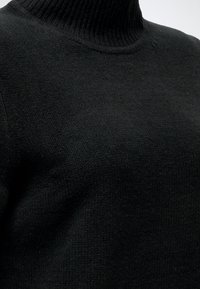 Gros plan d'un pull noir à col roulé en maille montrant un tissu texturé et un col côtelé.