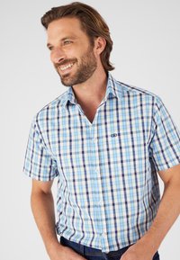 Camisa de cuadros de manga corta en tonos azul, blanco y amarillo; presenta un cuello abotonado y un detalle del logo en el pecho.