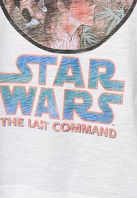 T-shirt bianco con il testo "STAR WARS" in blu e arancione in evidenza, e "THE LAST COMMAND" sotto, con un grafico di un personaggio al centro.