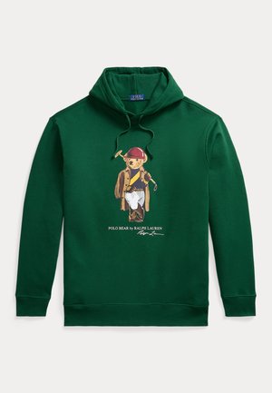 Zöld kapucnis pulóver macival, aki piros sisakot, kabátot és fehér nadrágot visel, valamint egy poloütőt tart a kezében, alatta a Polo Bear by Ralph Lauren felirat.