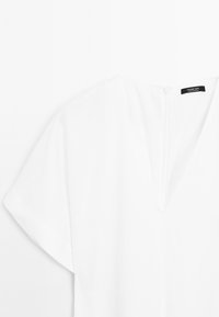 Blusa bianca con scollatura a V e maniche corte, con zip sul retro. Etichetta del marchio "Massimo Dutti" visibile sul capo.