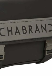 Schwarze, strukturierte Tasche mit einem grauen Tragegurt, auf dem das Wort "CHABRAND" in fetter Schrift steht. Metallakzente an dem Gurt.