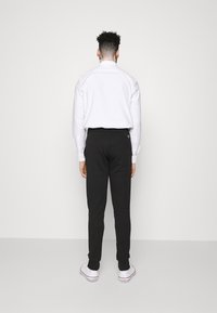 Bílá košile s dlouhým rukávem, černé tepláky a bílé tenisky. Košile má manžety na knoflíky a tepláky mají boční kapsu a slim fit střih.