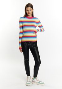 Daugiaspalvis struktūruotas megztinis su horizontaliomis raudonomis, mėlynomis ir geltonomis juostelėmis, derinamas su juodomis odinėmis kelnėmis ir pastelinėmis sportbačiais.