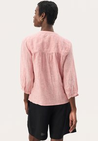 Lightweight, striped cotton blouse in coral and white with three-quarter sleeves and gathered back detail, paired with black shorts.