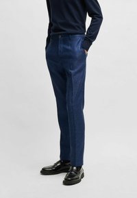 Navy blue trousers with a textured finish, featuring a flat front, side pockets, and a tailored fit, paired with black shoes.