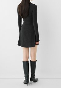 Långärmad klänning i kolgrått med en utsvängd kjol. Matchad med knähöga, blanka svarta stilettstövlar. Slät textur genom hela outfiten.