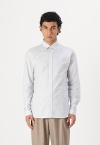 Cămașă cu dungi, în nuanțe de albastru deschis și alb, din material de bumbac, cu tăietură slim, guler clasic și mâneci lungi. Pantaloni într-o nuanță neutră.