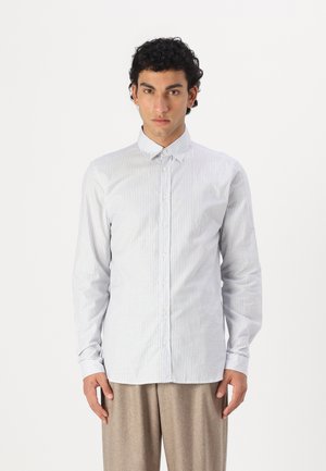 Camisa de botones a rayas en azul claro y blanco, de material de algodón, corte ajustado, con collar clásico y mangas largas. Pantalones en un tono neutro.