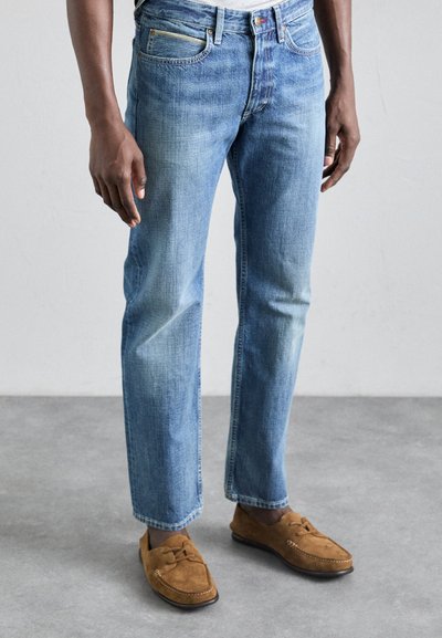 Light blue denim jeans with a straight fit, subtle fading, and five-pocket design, paired with brown suede loafers.