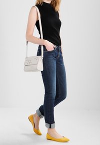 Svart ribbad ärmlös topp, blå jeans med upprullade muddar, gula ballerinaskor och en vit axelremsväska med blommiga detaljer.