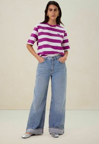 Gestreept paarse en witte t-shirt met korte mouwen, gecombineerd met lichtblauwe high-waisted wijde jeans en zilveren platte schoenen.