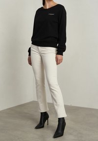 Schwarzer Sweatshirt mit gerippten Bündchen, cremefarbene gerade Jeans und schwarze spitze Stiefeletten. Einfaches Design mit einem Logo auf der Brust.
