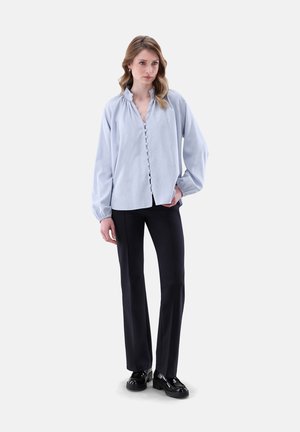 Blusa azzurra chiara con colletto arricciato e maniche ampie, abbinata a pantaloni neri e scarpe nere lucide.