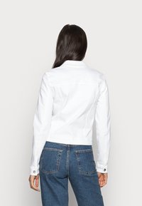 Bílá džínová bunda se slim fit střihem, límečkem a knoflíkovými manžetami. Zadní strana má krejčovsky šité švy a zkrácenou délku.