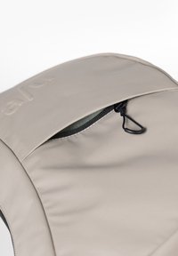 Beige fabric backpack pocket with black zipper partially open and a black pull loop on a white background.
