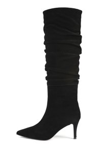 Bota negra de ante hasta la rodilla con punta afilada, caña holgada y tacón delgado de altura media.