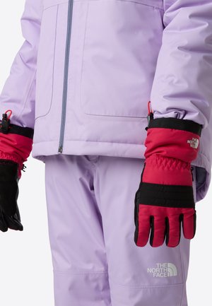 Lila Außenjacke mit Reißverschluss, kombiniert mit rot-schwarzen, isolierten Handschuhen mit Logo und strukturierten Stoffakzenten.