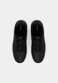 Juoda pora batų su raišteliais ir baltais padais, matoma iš viršaus ant paprasto balto fono.