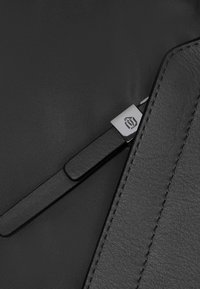 Custodia per laptop nera con dettagli in pelle liscia e logo metallico. Presenta una superficie in tessuto testurizzato e una cucitura precisa.